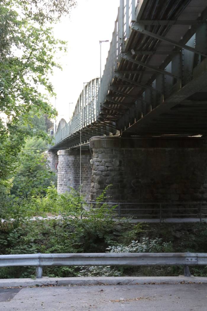 Blick vom Ufer auf einen Steinpfeiler und die Unterseite der Eisenbahnbrücke